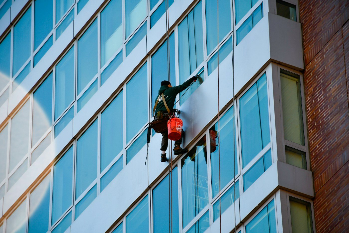 Professional high-rise window cleaner secured on a modern glass building